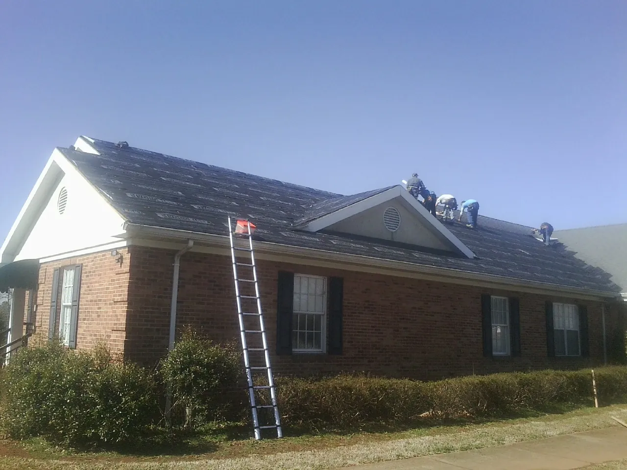 Crew tearing shingles off a brick ranch roof with a ladder set — Metal Roof Repair work by our crew in Mahopac Falls