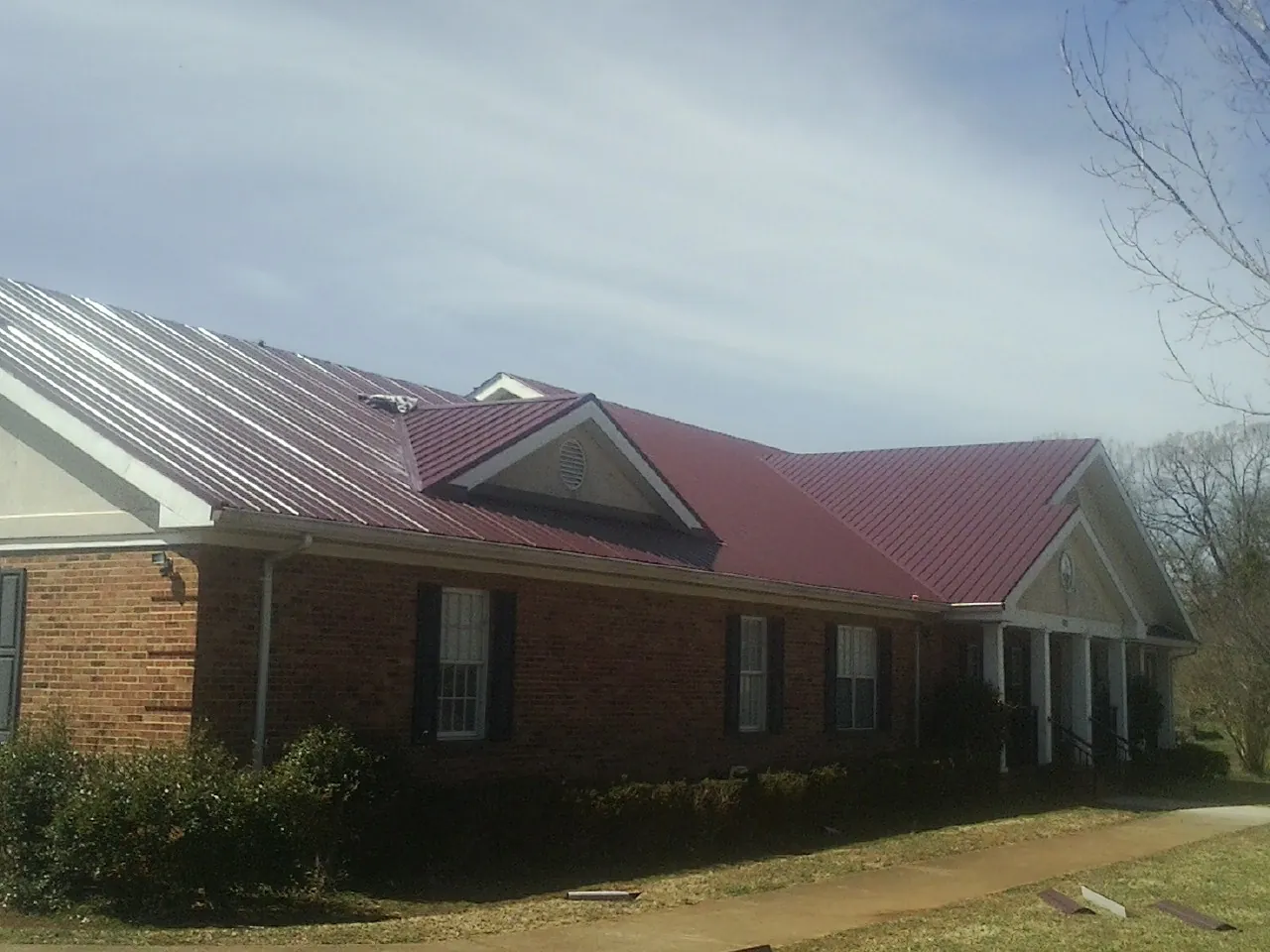 Red metal roof with gabled entries on a long brick building, from a Hail Damage Roof Repair job in Mahopac Falls