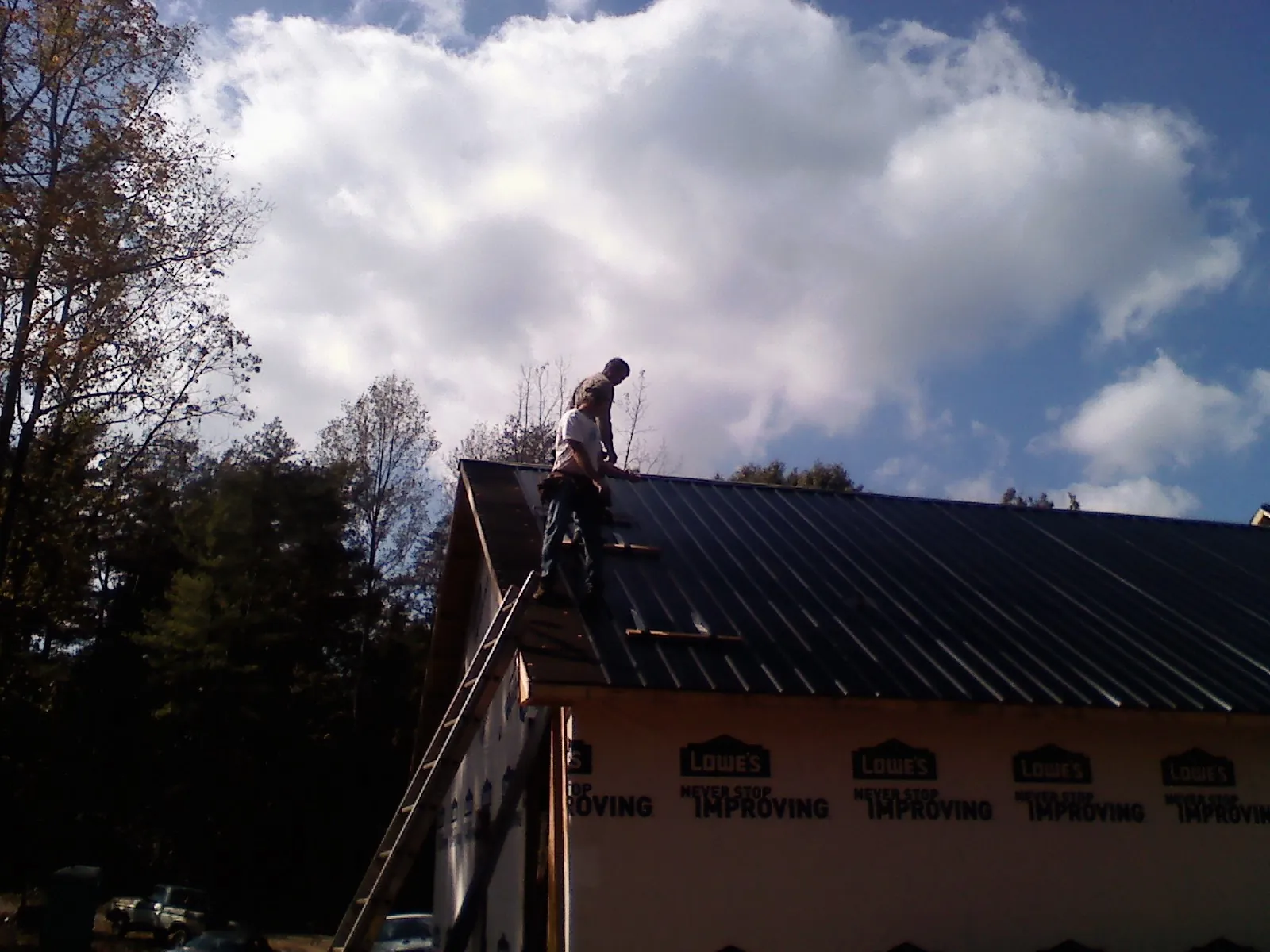 Roofer fastening dark metal panels high against a cloudy sky, from a Roof Inspection job in Mahopac Falls