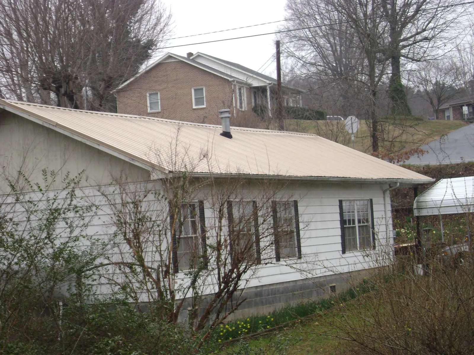 Tan metal roof on a white sided house set into a hillside — Commercial Roofing by Roofing Brothers in Mahopac Falls